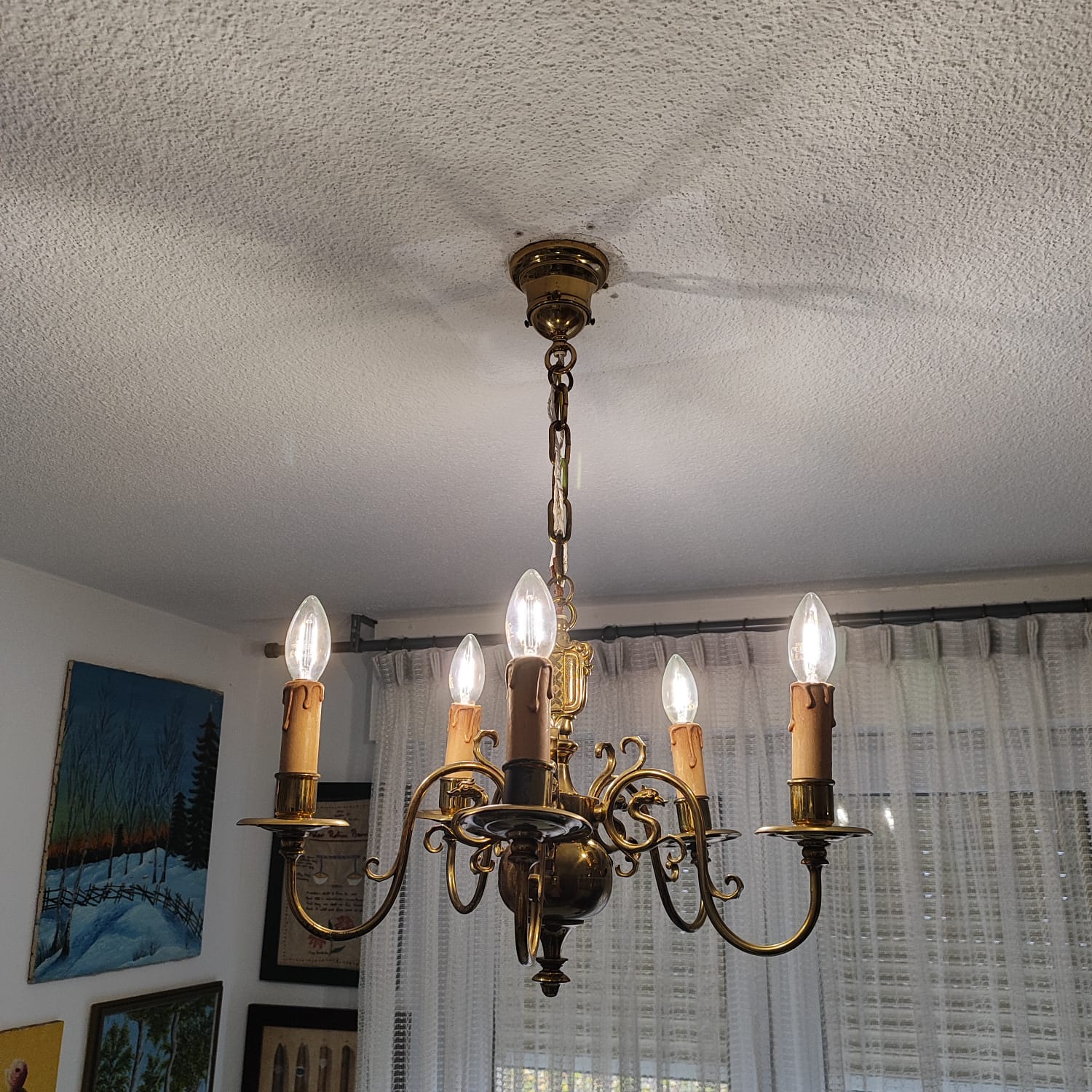 Lustre en laiton à cinq bougies installé au plafond d'un séjour avec rideaux